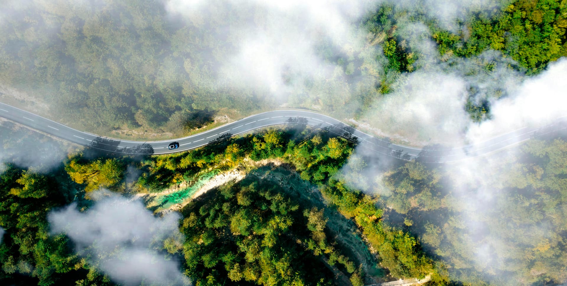 Malerische Luftaufnahme eines Autos, das durch neblige bewaldete Berge fährt, symbolisiert Solavitas Mission für saubere Energie und Engagement für nachhaltige und umweltfreundliche Lösungen.