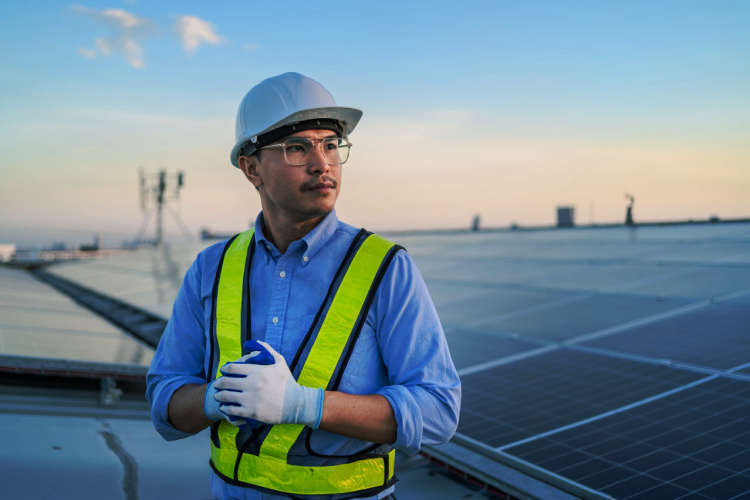 Techniker in Schutzausrüstung bei der Inspektion einer Solavita-Wechselrichter-Installation an einer Solarmodulreihe, mit Fokus auf die Sicherstellung der optimalen Systemleistung.